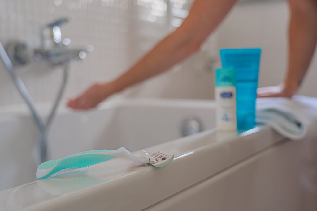 Close-up of shaving razor on bathtub edge with faucet in background, illustrating personal grooming.